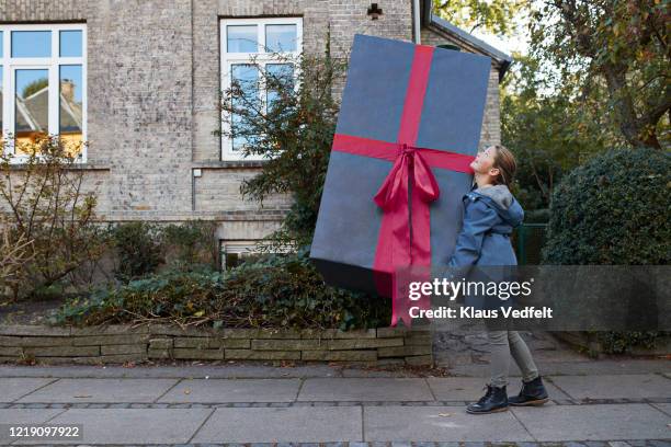 girl carrying large gift box on footpath in city - groot stockfoto's en -beelden