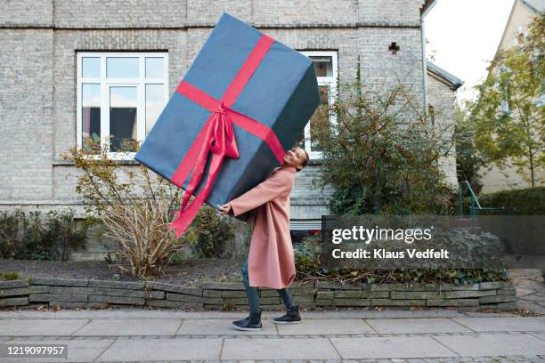 smiling woman carrying large gift box on footpath - funny gifts stock-fotos und bilder