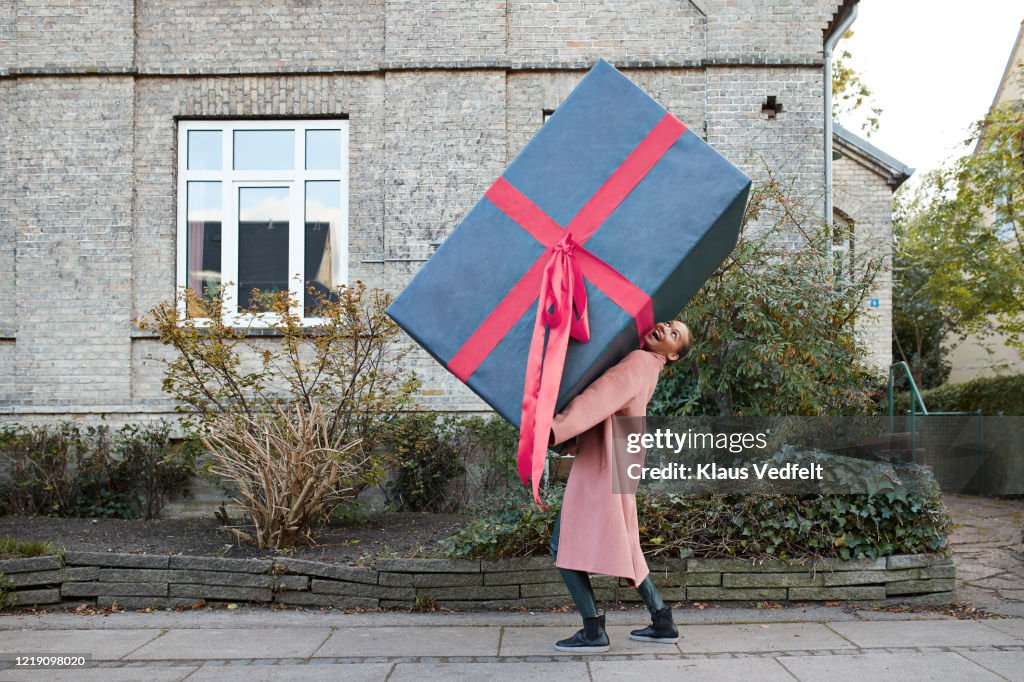 Happy woman carrying large gift box on footpath