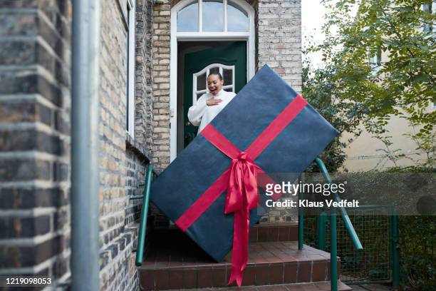 surprised woman looking at large gift box at entrance of house - blue house red door stock pictures, royalty-free photos & images