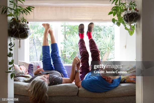 a senior couple lie on the sofa with their legs in the air - couple de vieux drole photos et images de collection