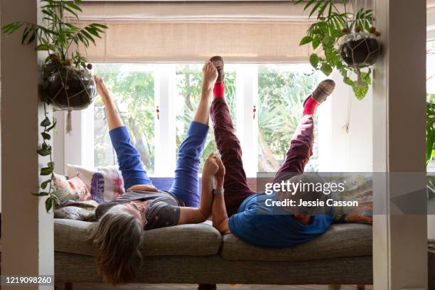 a senior couple lie on the sofa with their legs in the air - lockdown window stock pictures, royalty-free photos & images