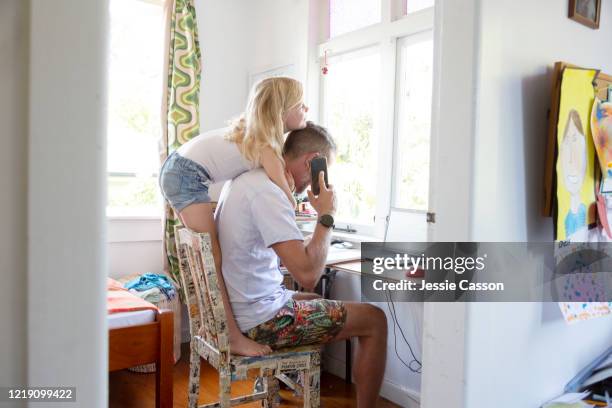 a girl hugs her dad while he is on a phone call at home - auckland city busy stockfoto's en -beelden