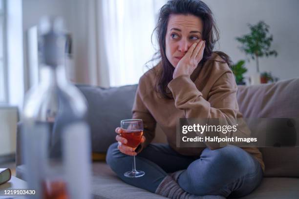 sad and depressed woman sitting indoors on sofa, holding glass of wine. - drinking alcohol at home stock pictures, royalty-free photos & images