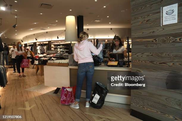 An employee wearing a protective face mask rings up a customer at a cash register behind a plexiglass barrier at at an Abercrombie & Fitch store...