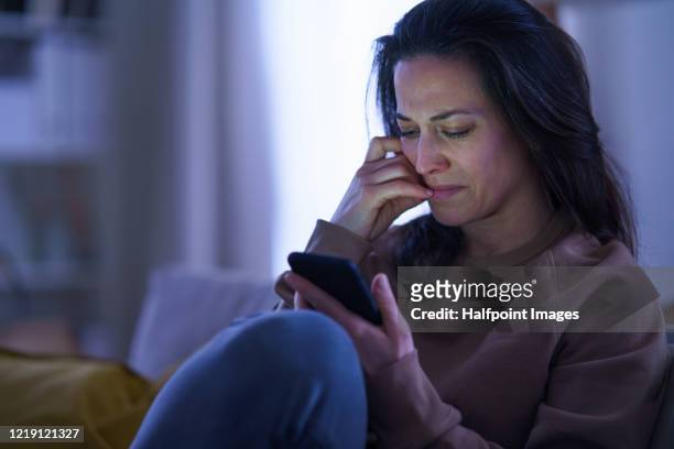 sad and depressed woman indoors at home, using smartphone. - overstuur stockfoto's en -beelden