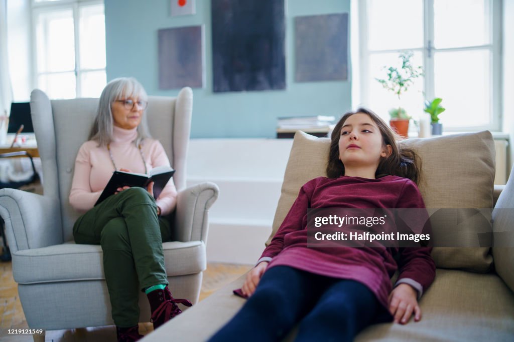 Sad and depressed small girl with therapist sitting indoors, psychotherapy.