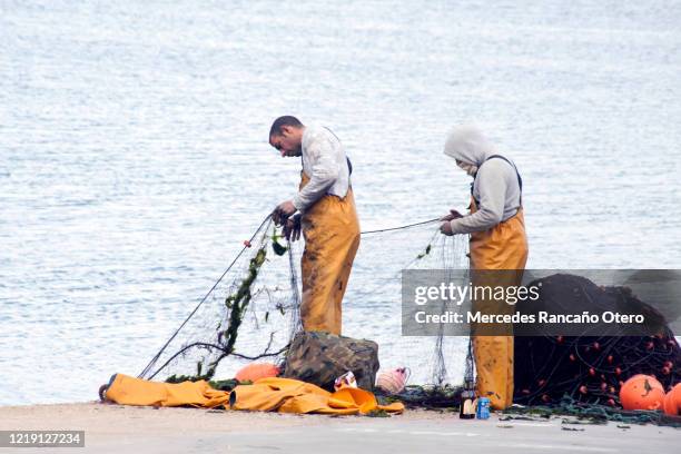 dos pescadores reparando redes de pesca en un muelle. - commercial fishing net fotografías e imágenes de stock