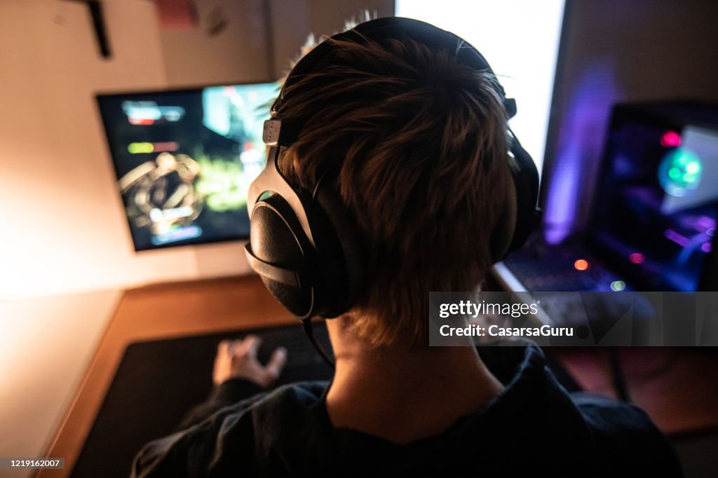 Vista trasera de Gamer con auriculares al jugar videojuegos en línea en Dark Room - foto de archivo