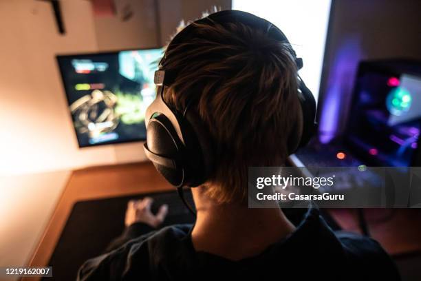 rear view of gamer with headset on playing online video games in dark room - stock photo - addict stock pictures, royalty-free photos & images