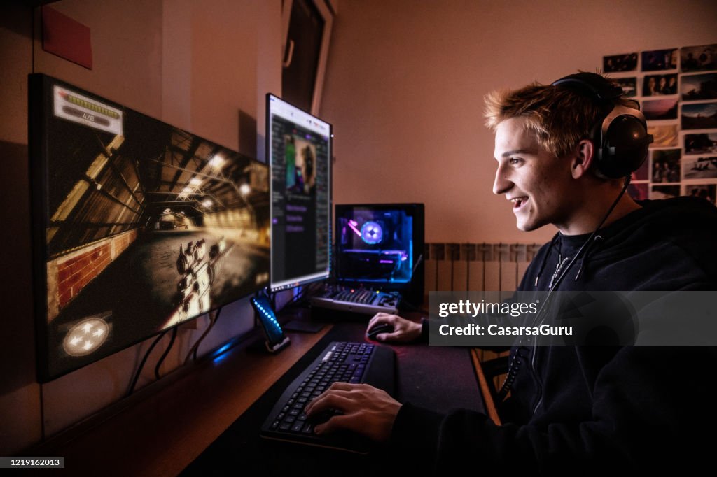 Young Man Enjoying Playing Online Multiplayer Games with his Friends while Locked in Quarantine - stock photo