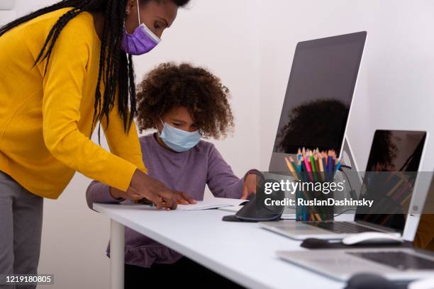 a private teacher woman helping 6 years old school child to read. both are wearing face masks, reading, studying, using an exercise book, pencils, computers, and the internet. coronavirus pandemic education concept. - 6 7 years stock pictures, royalty-free photos & images