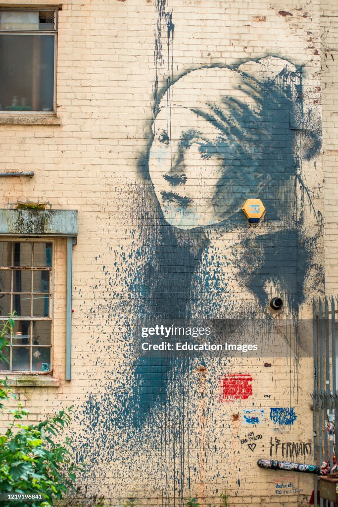 Girl with a pierced eardrum, an artwork based around a burglar alarm by artist Banksy on the wall of an alley in Albion Docks, Bristol, England, UK