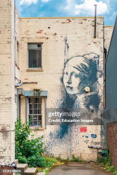Girl with a pierced eardrum, an artwork based around a burglar alarm by artist Banksy on the wall of an alley in Albion Docks, Bristol, England, UK.