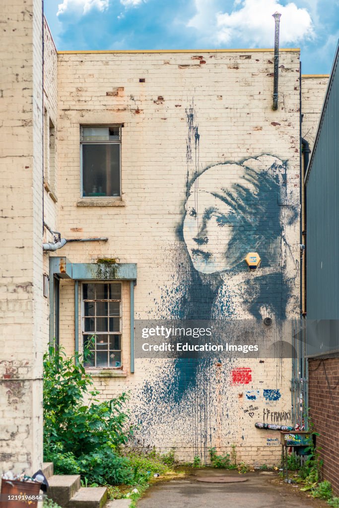 Girl with a pierced eardrum, an artwork based around a burglar alarm by artist Banksy on the wall of an alley in Albion Docks, Bristol, England, UK