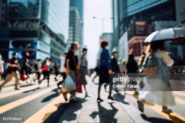 defocused image of commuters with protective face mask to protect and prevent from the spread of viruses during the coronavirus health crisis, crossing street in busy downtown district against corporate skyscrapers - mask culture stock-fotos und bilder