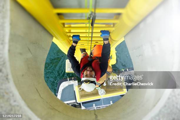 alto lavoratore manuale arrampicata offshore su turbina eolica su scala e nave di trasferimento in attesa sotto turbina eolica - torre struttura edile foto e immagini stock