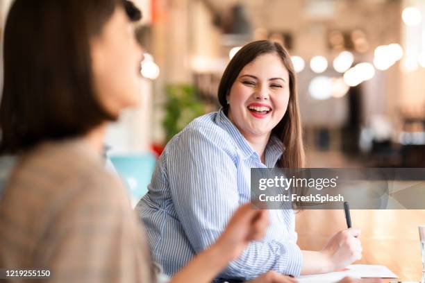 fun times at work: young plus size femme d’affaires partageant un rire avec un collègue au bureau - mannequin grande taille photos et images de collection