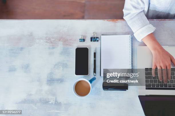 vista dall'alto della donna che usa il laptop mentre è seduta al tavolo con laptop, telefono cellulare, blocco note vuoto e penna. - office work flat lay foto e immagini stock