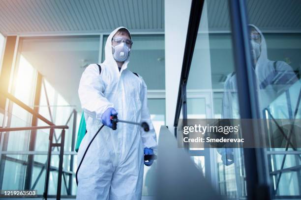 Shot of male person in white chemical protection suit doing disinfection of public areas to stop spreading highly contagious corona virus. Stop coronavirus or COVID-19.