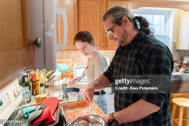 father, a middle-aged 50-years-old man wearing a ponytale greasing a pan for a pie that his adolescence daughter is preparing. - 16 17 years imagens e fotografias de stock