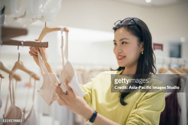 衣料品店で新しいブラジャーを選ぶ若いアジアの女性。 - ブラジャー ストックフォトと画像