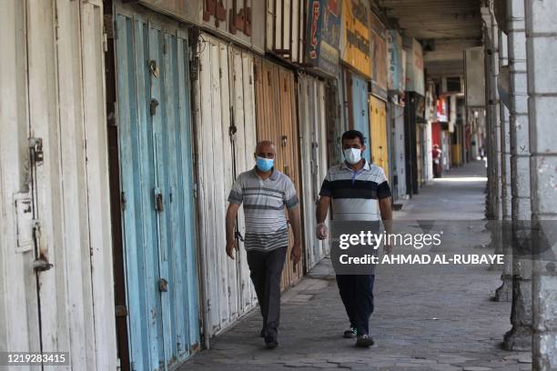 Iraqi men wearing protective masks walk through an empty commercial street on June 11, 2020 in central Baghdad during restrictions on movement due to...