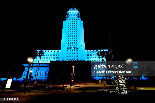 View of Los Angeles City Hall illuminated in blue on April 16, 2020 in Los Angeles, United States. Landmarks and buildings across the nation are...