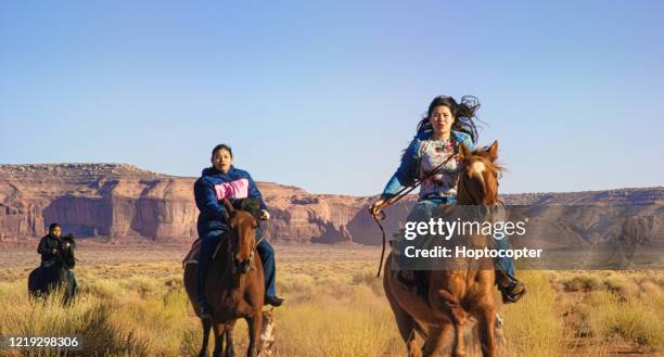 teenaged native american children (navajo) gallop on their horses through the monument valley desert in arizona/utah on a sunny afternoon - horseback riding arizona stock pictures, royalty-free photos & images