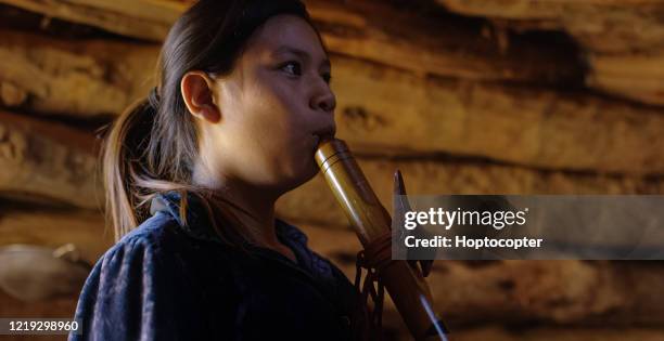 a teenaged native american girl wearing traditional navajo clothing plays a navajo flute in a hogan (navajo hut) stock - native american music stock pictures, royalty-free photos & images
