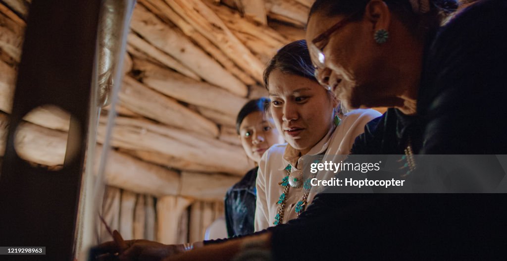 A Native American Grandmother (Navajo) in Her Sixties Teaches Her Teenaged Granddaughters How to Weave at a Loom Indoors in a Hogan (Navajo Hut)
