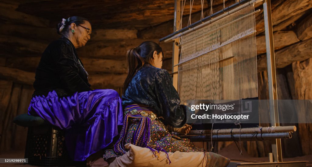 A Native American Grandmother (Navajo) in Her Sixties Teaches Her Teenaged Granddaughter How to Weave at a Loom Indoors in a Hogan (Navajo Hut)