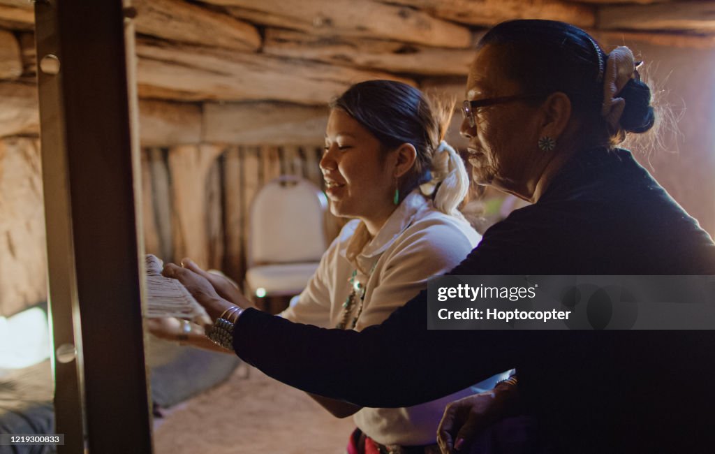 A Native American Grandmother (Navajo) in Her Sixties Teaches Her Teenaged Granddaughter How to Weave at a Loom Indoors in a Hogan (Navajo Hut)