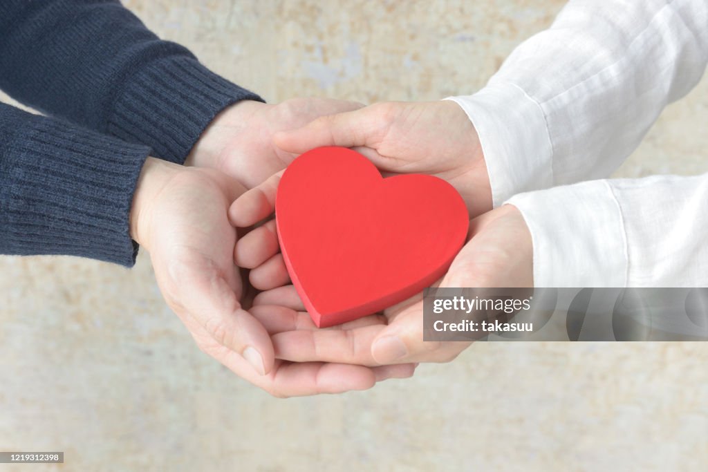 Herzobjekt mit männlichen und weiblichen Händen bedeckt