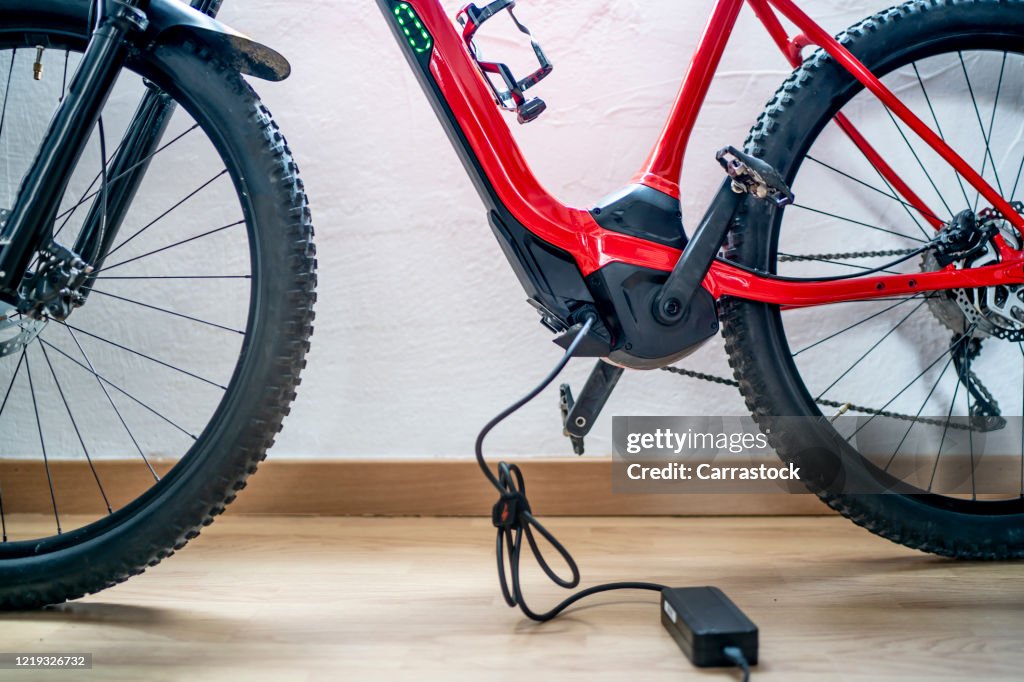 Electric mountain bike charging battery next to home window.