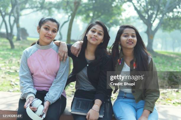 group of multi ethnic happy female friends sitting on a bench in the park and enjoying in nature. - three young women stock pictures, royalty-free photos & images