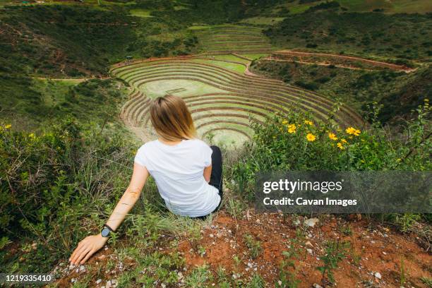 a young woman is sitting near the famous peruvian spot moray in peru - moray cusco fotografías e imágenes de stock