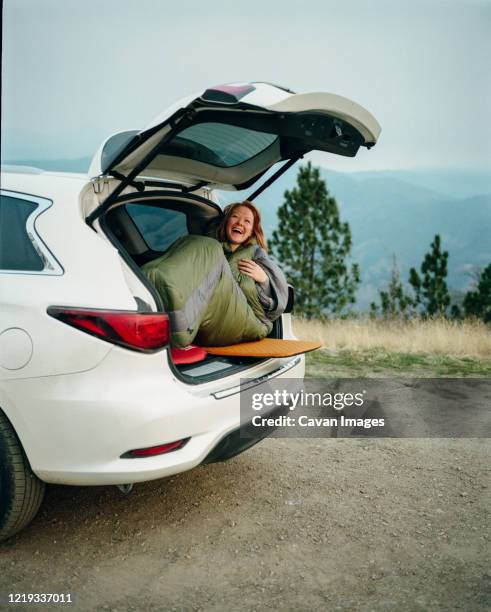 woman in sleeping bag laughing while car camping in big sur - compact car stock pictures, royalty-free photos & images