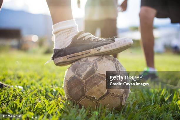 soccer (football) player places old shoe on torn soccer ball. - boys sport pants stock pictures, royalty-free photos & images