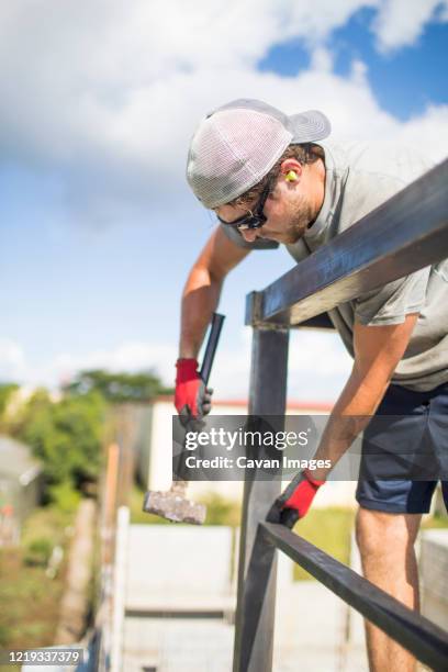 construction worker using hammer to build steel railing on roof. - positioning welding stock pictures, royalty-free photos & images