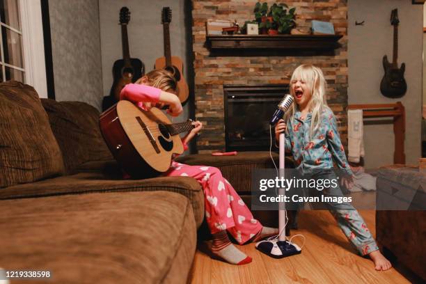 young girls singing loudly and playing guitar in living room - saiteninstrument spielen stock-fotos und bilder