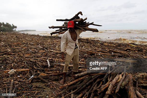 Man collects wood from a beach carpeted with debris in the battered town of Nagua on August 23, 2011 as winds and rain of Hurricane Irene are still...
