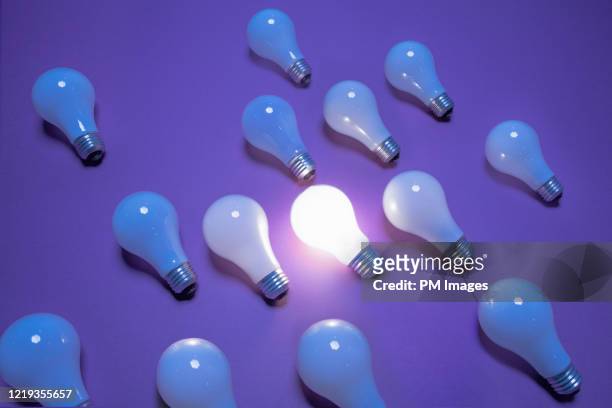 one lit lightbulb among many - idea bulb stockfoto's en -beelden