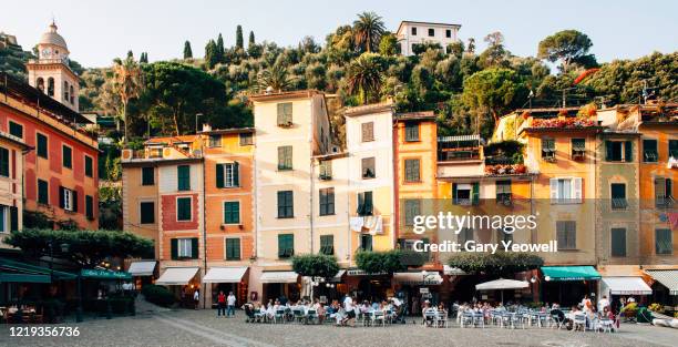 people sitting outside restaurants in a piazza - portofino foto e immagini stock