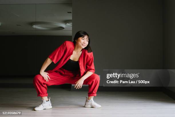 young woman in red clothing crouching while posing for portrait in empty room - red pants - fotografias e filmes do acervo