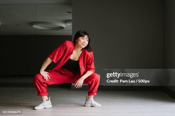 young woman in red clothing crouching while posing for portrait in empty room - röda byxor bildbanksfoton och bilder