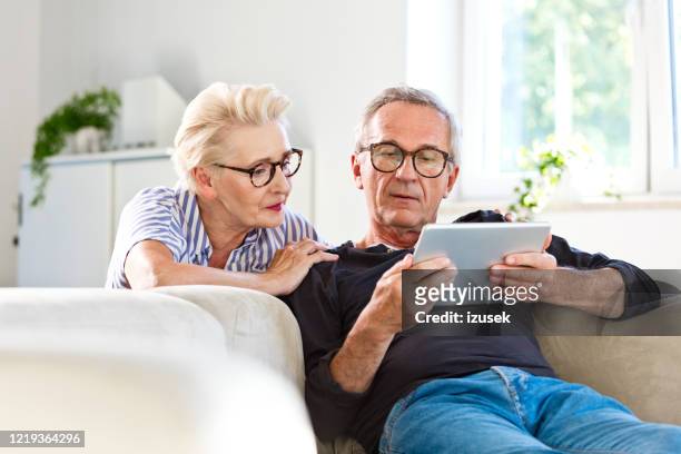 couples aîné regardant la tablette numérique ensemble à la maison - saving photos et images de collection
