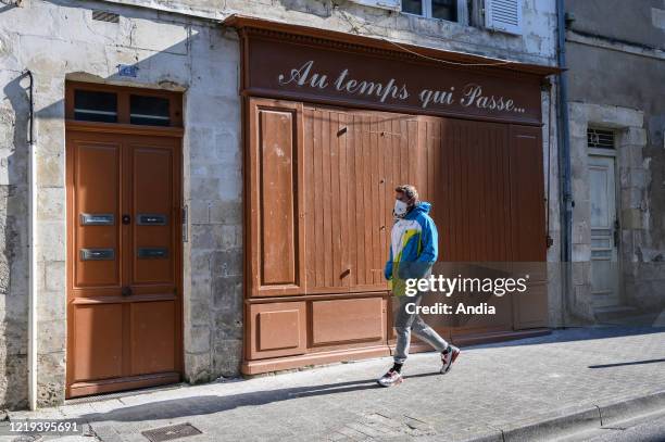 La Rochelle on April 2, 2020: coronavirus outbreak and quarantine. Man wearing a mask walking past the window of the coffee shop 'Le temps qui passe'.