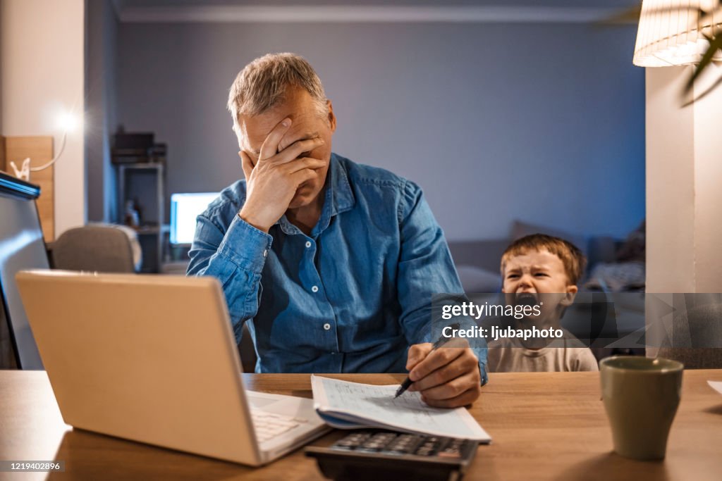 Gestresster Mann mit seinem zweijährigen Sohn arbeiten von zu Hause aus