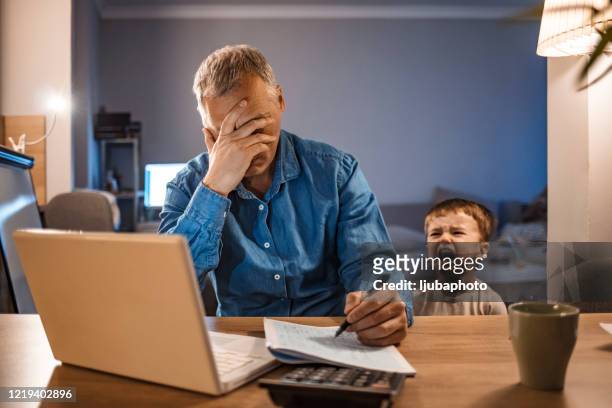 hombre estresado con su hijo de dos años trabajando desde casa - frustración fotografías e imágenes de stock